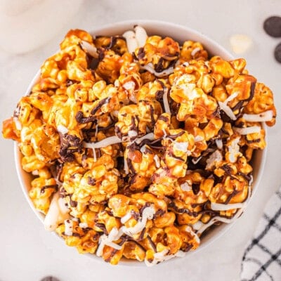 top down look at caramel corn in white bowl on marble surface. popcorn has been drizzled with white and dark chocolate.