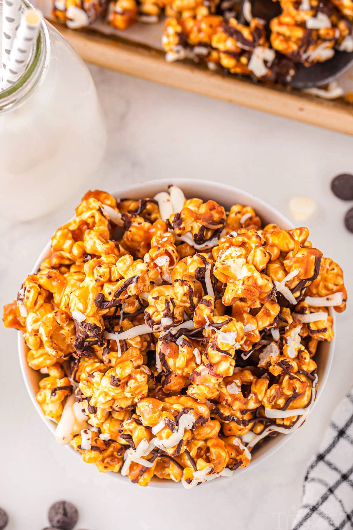 top down look at caramel corn in white bowl on marble surface. popcorn has been drizzled with white and dark chocolate.