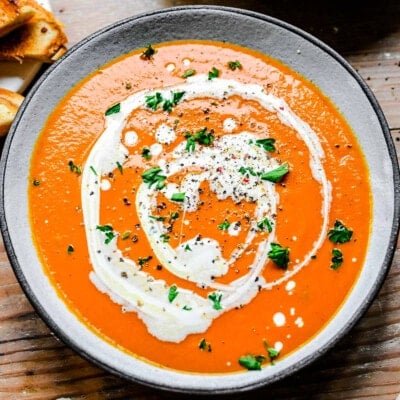 bowl of tomato soup drizzled with heavy cream, chopped basil sprinkled on top.