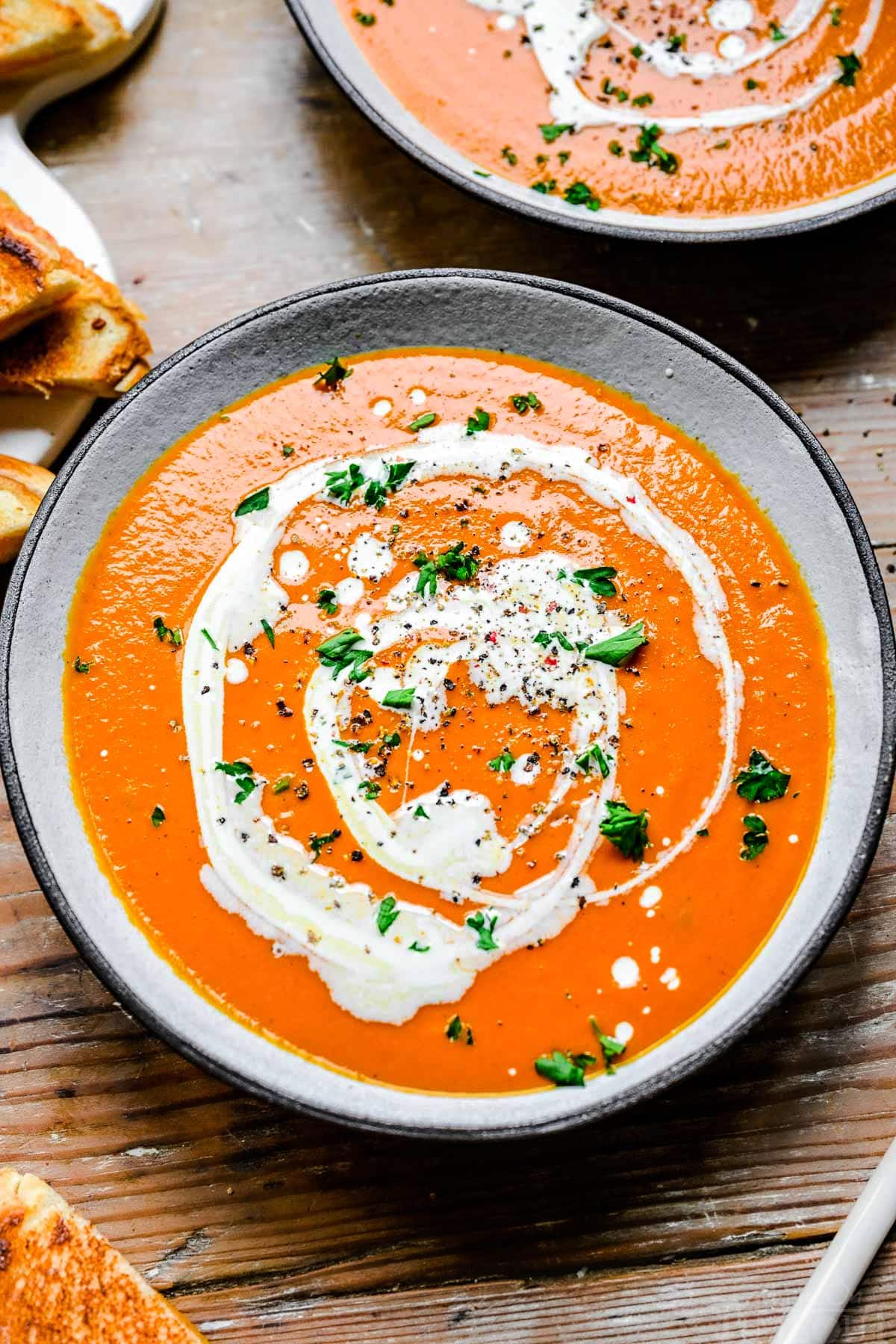 bowl of tomato soup drizzled with heavy cream, chopped basil sprinkled on top.
