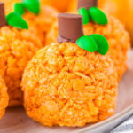 pumpkin shaped rice krispie treats sitting on a round white plate with a striped napkin next to them.