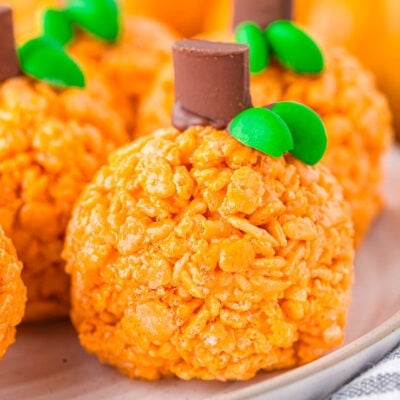 pumpkin shaped rice krispie treats sitting on a round white plate with a striped napkin next to them.