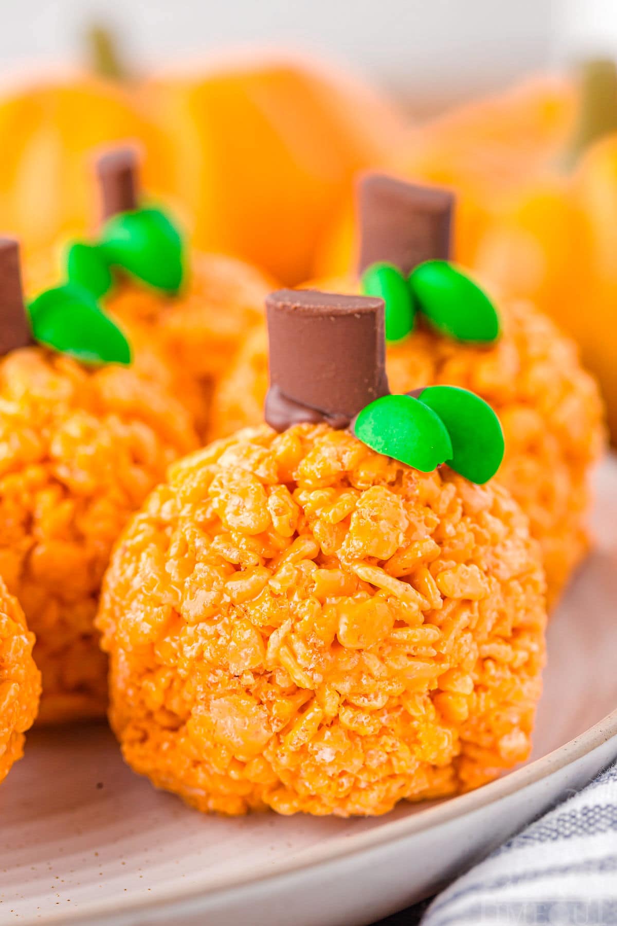five or six pumpkin shaped rice krispie treats sitting on a round white plate with a striped napkin next to them.