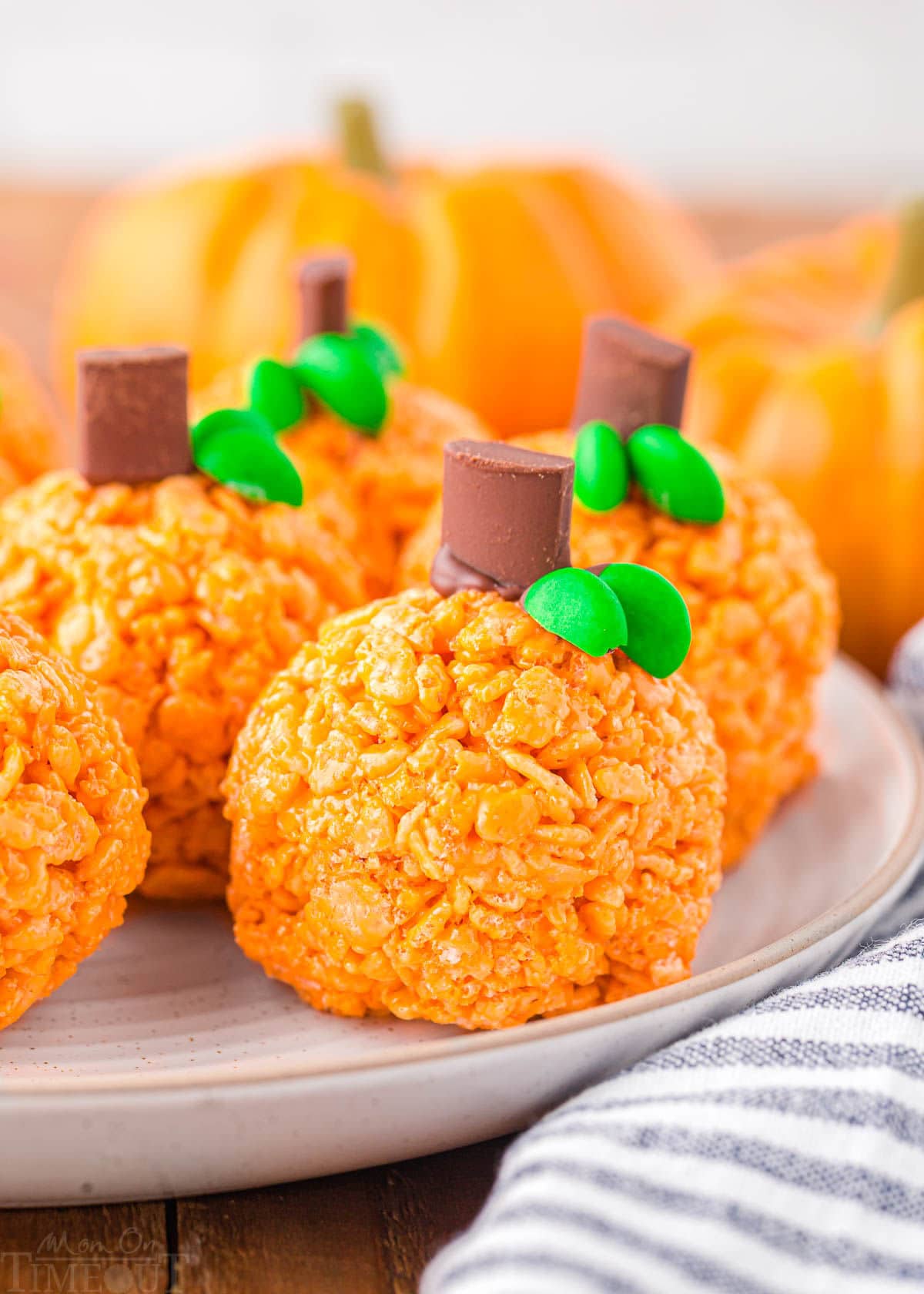 five or six pumpkin shaped rice krispie treats sitting on a round white plate with a striped napkin next to them.