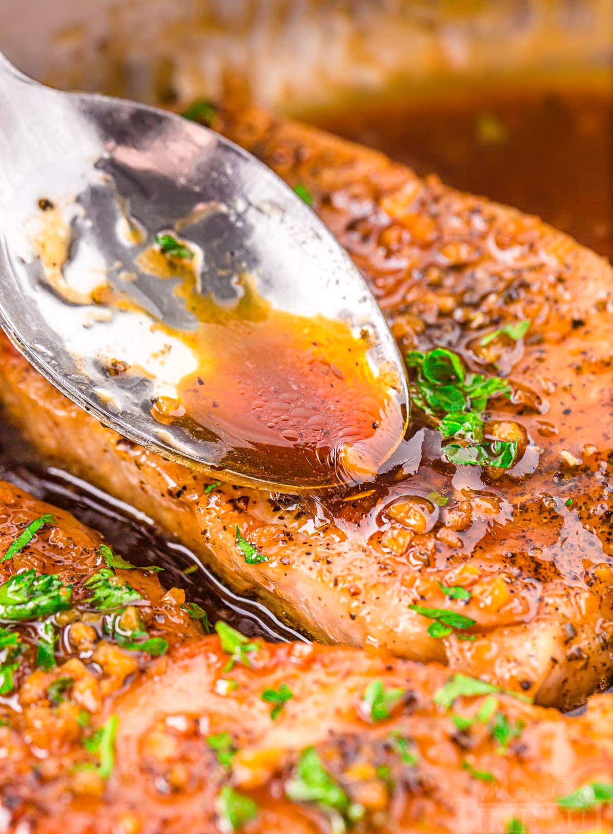 spoonful of glaze being spooned onto a pork chop in a skillet.