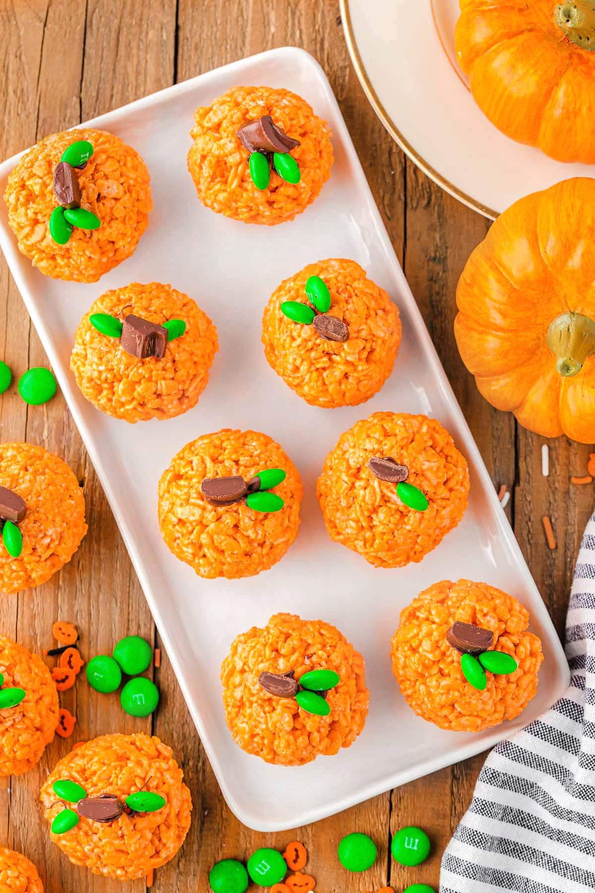 top down view of pumpkin rice krispie treats on large rectangular white platter with some decorative pumpkins to the side.