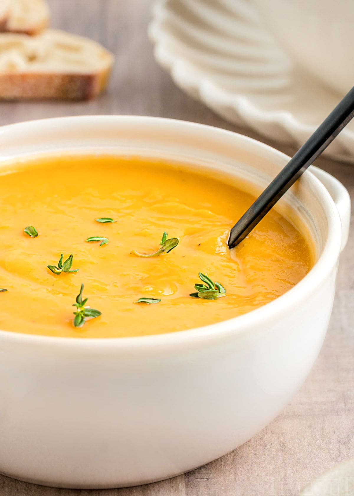 close up look at butternut squash soup with bright orange color in white bowl topped with fresh thyme.
