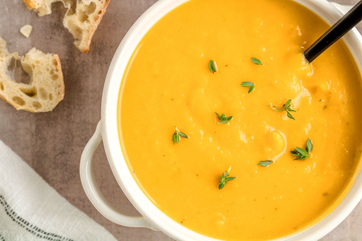 top down shot of roasted butternut squash soup in bright white round bowl topped with fresh thyme.