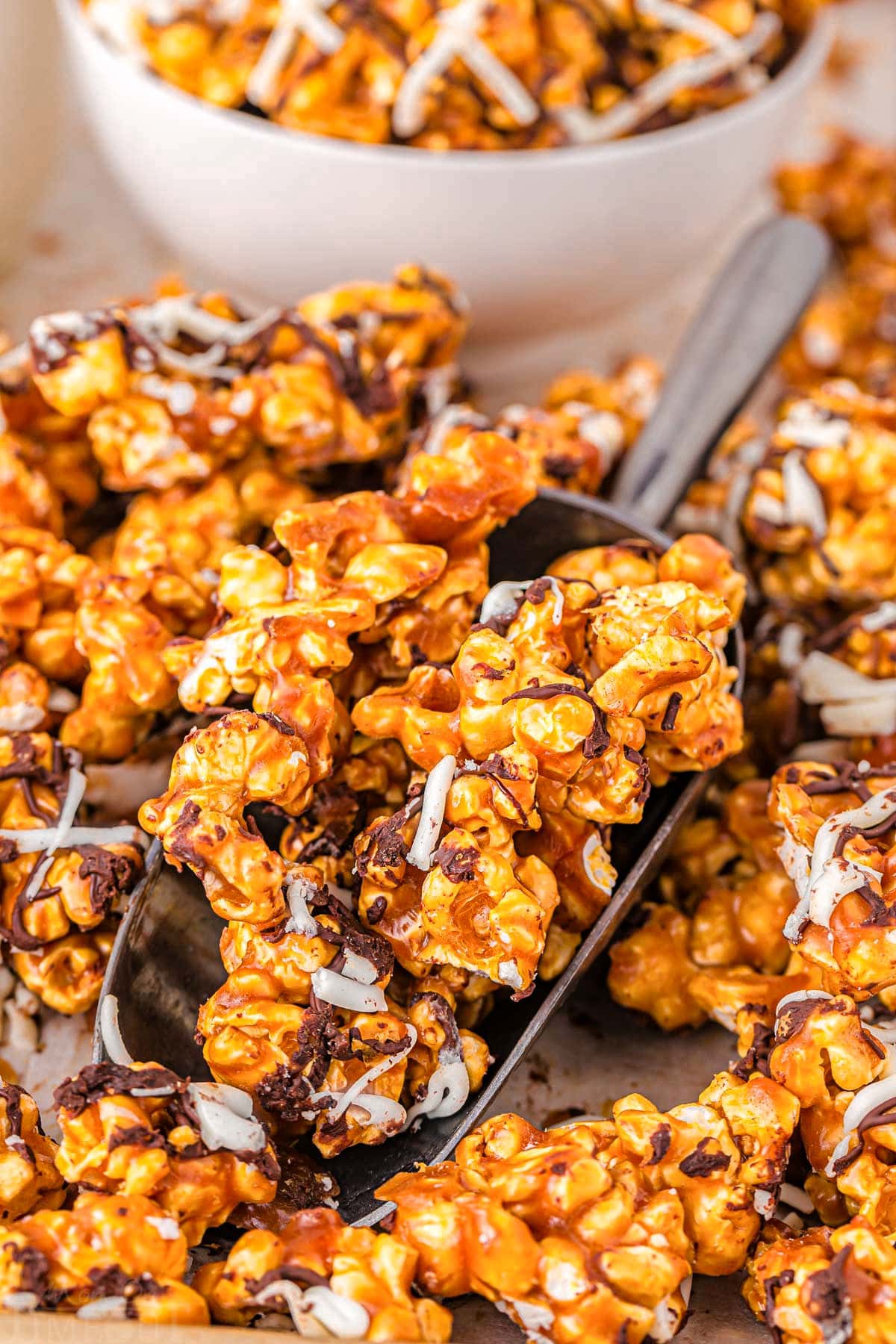 large metal scoop scooping up caramel corn off of sheet tray. white bowl can be seen in the background.