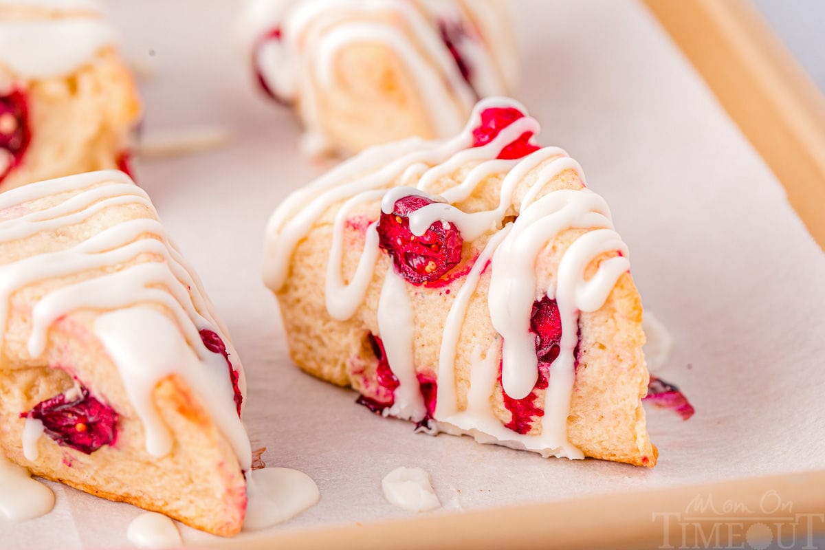 four cranberry scones on a parchment lined baking sheet topped with a simple glaze. 