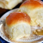 two fluffy dinner rolls sitting on a round white plate with gold trim.