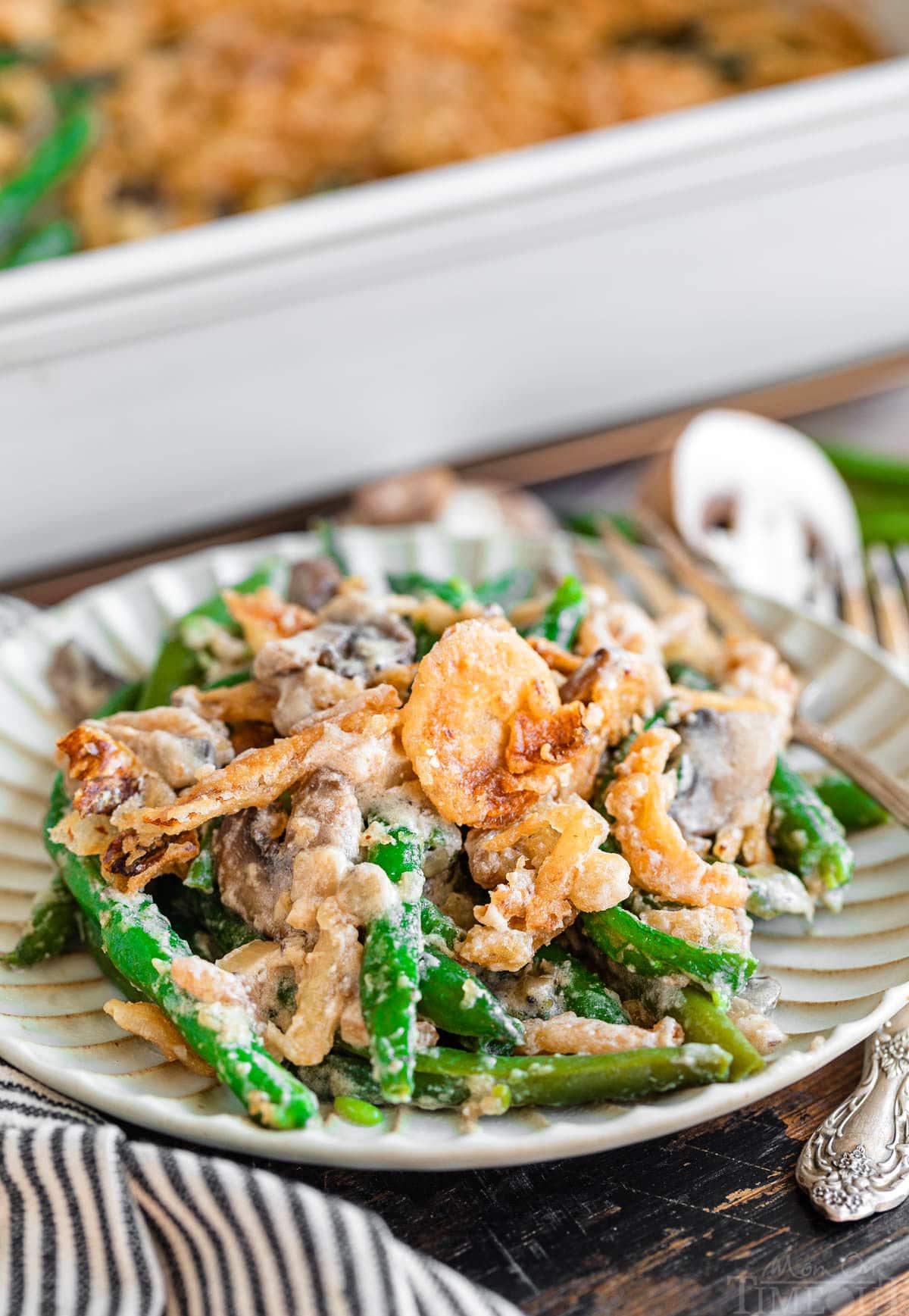 small plate with one serving of green bean casserole recipe on it with casserole dish in the background.