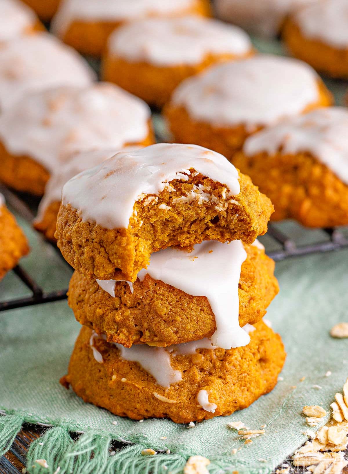 three iced pumpkin cookies stacked with top cookie has a bite removed.