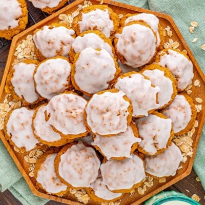 top down look at octagon shaped wood tray stacked high with pumpkin oatmeal cookies that have been iced. a green napkin is underneath the tray.