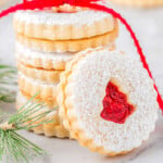 stack of linzer cookies with raspberry jam tied with red ribbon. one cookie is leaning up against the stack.