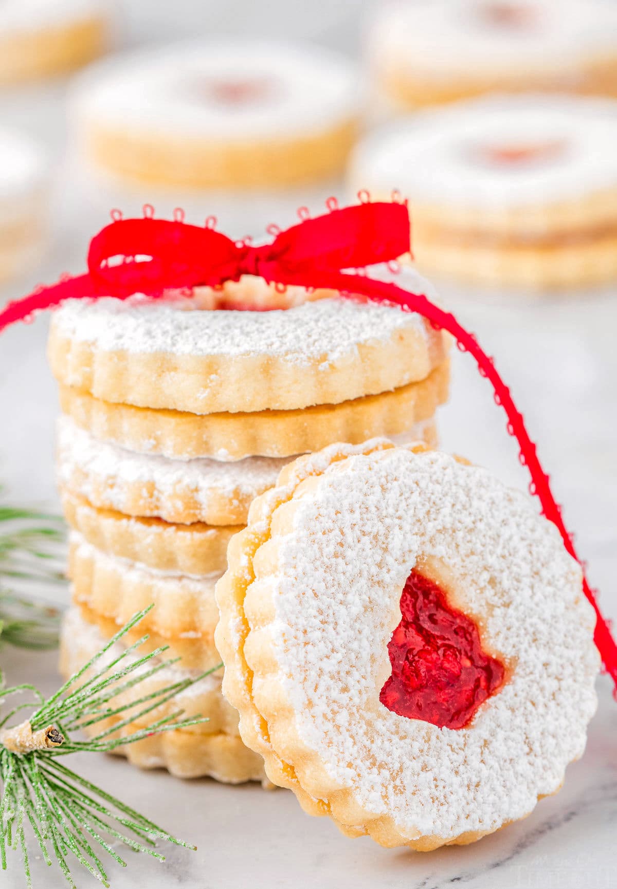 stack of linzer cookies with raspberry jam tied with red ribbon. one cookie is leaning up against the stack.