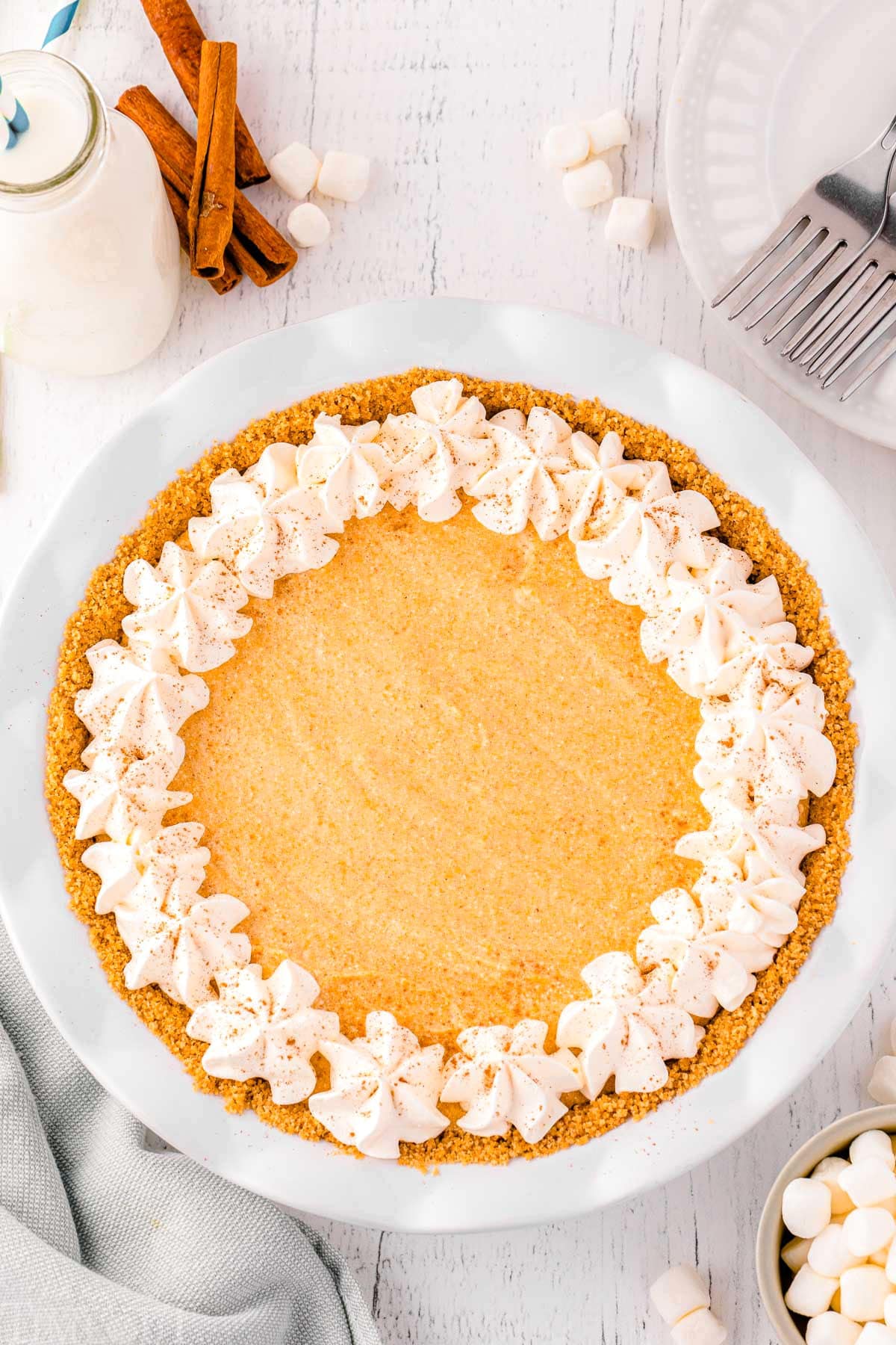 top down view of whole no bake pumpkin pie sitting on marble surface next to cinnamon sticks.