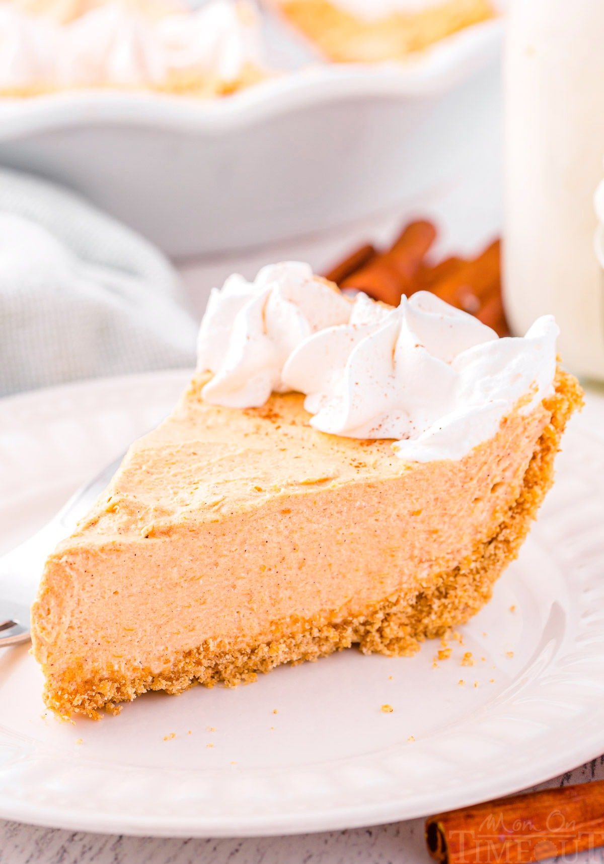 slice of no bake pumpkin pie on a white plate topped with whipped cream. 