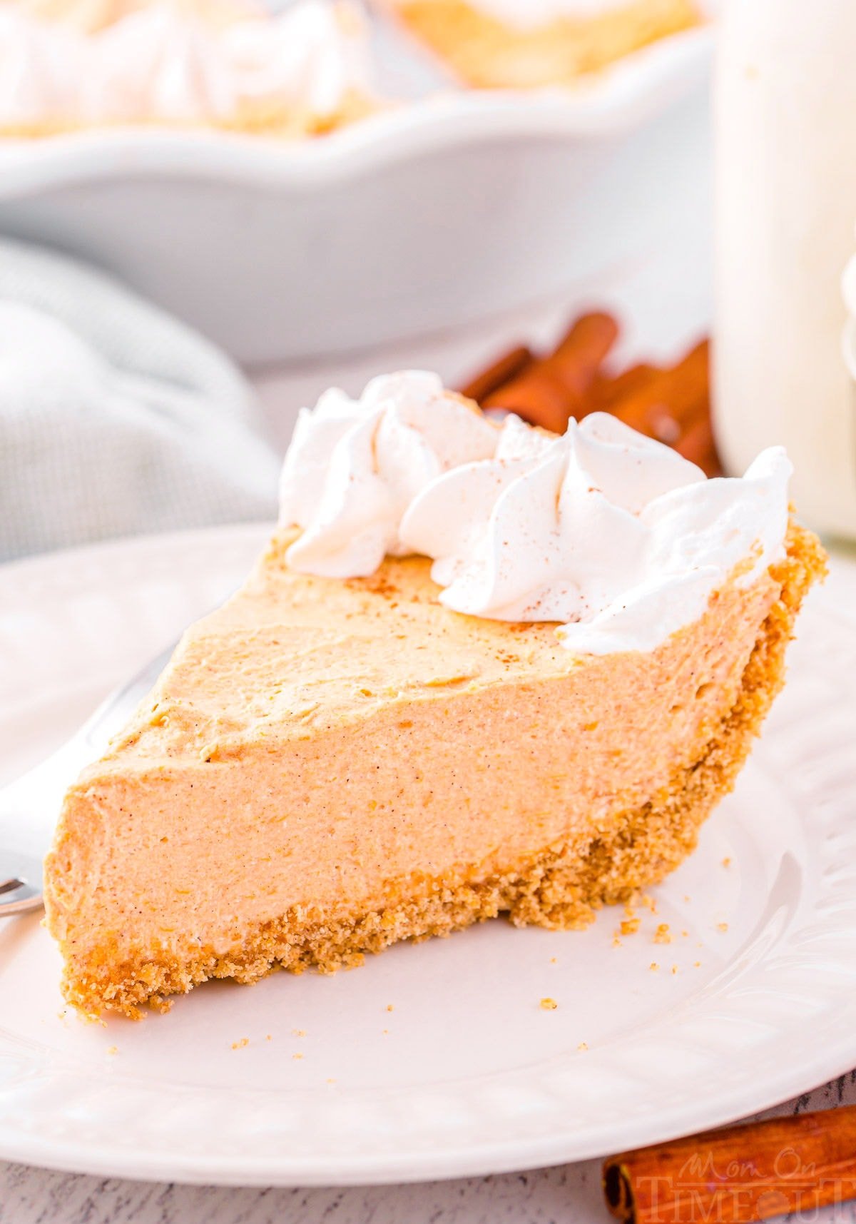 slice of no bake pumpkin pie on a white plate topped with whipped cream.