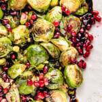 Top down view of roasted brussels sprouts on a pink and white serving dish. the sprouts are topped with pomegranate seeds and thyme along with a balsamic glaze.