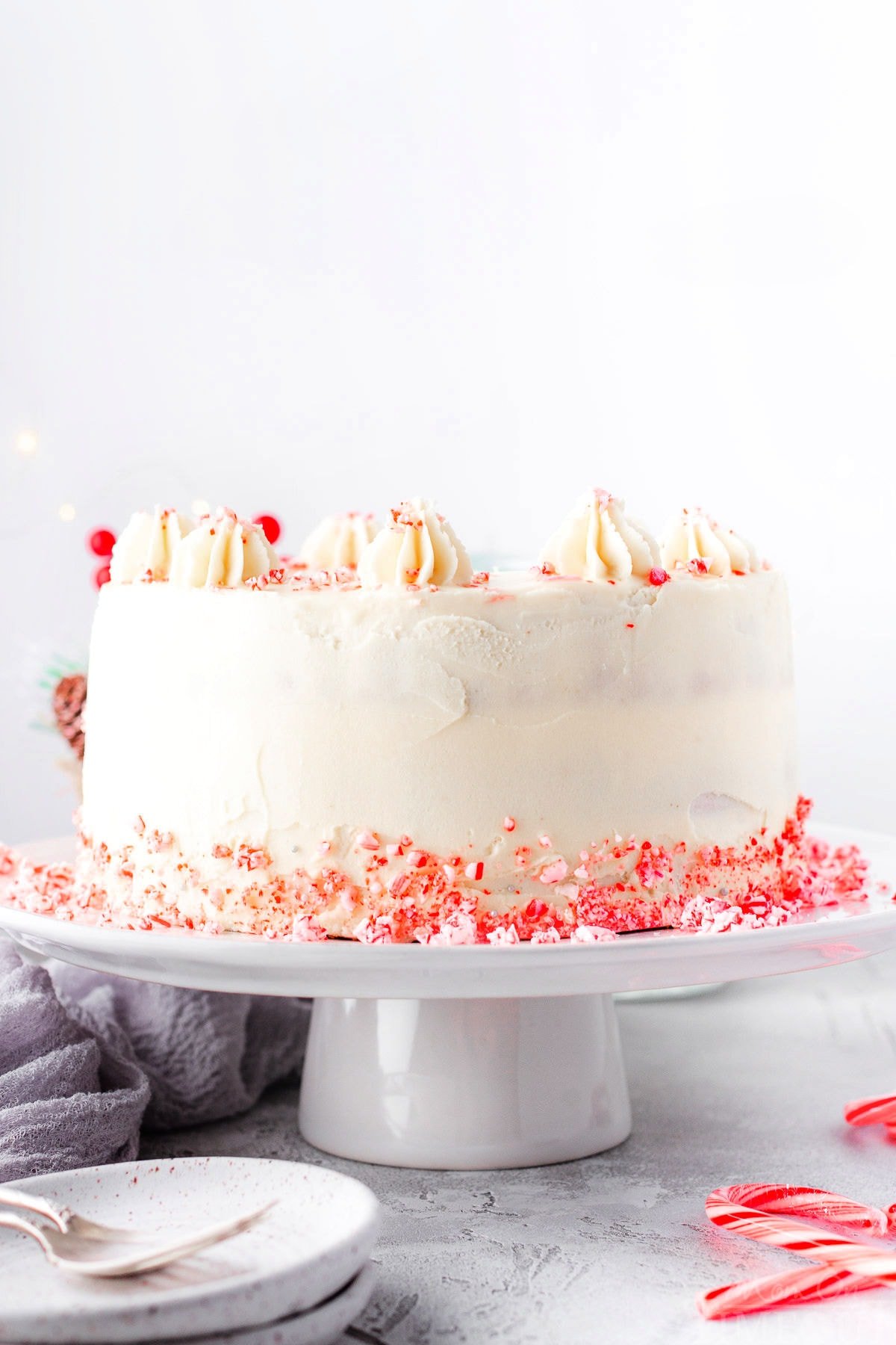 whole peppermint cake on a white cake stand with candy canes crumbles around the base.