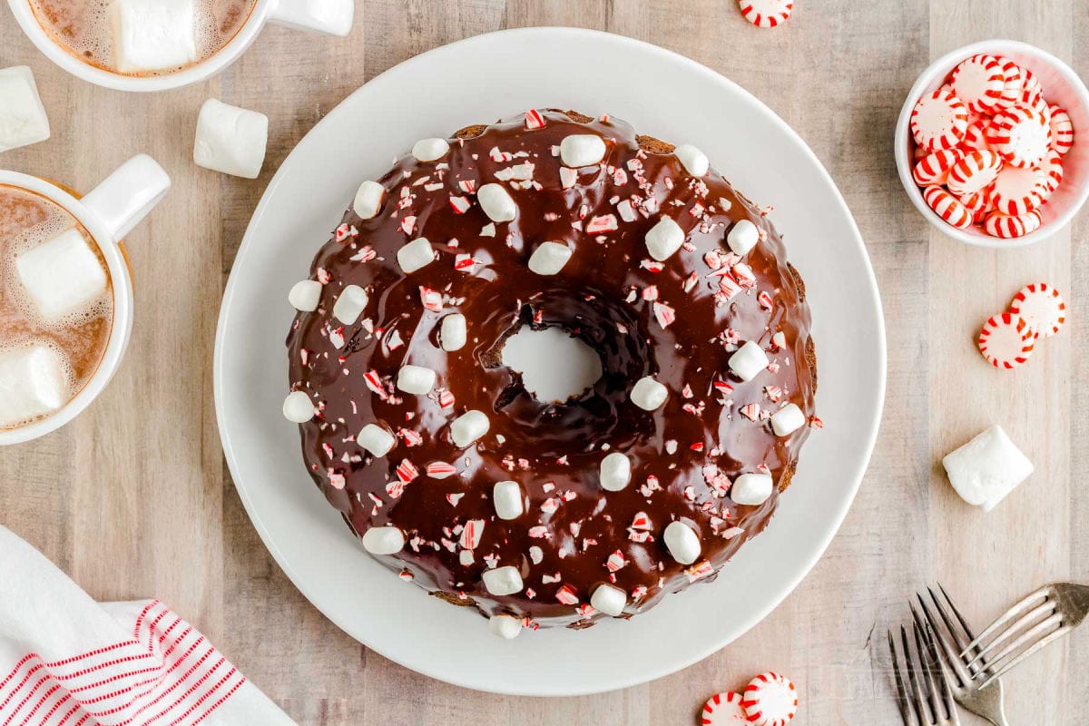 top down look at a chocolate bundt cake decorated with marshmallows and crushed peppermint candy. the cake is on a white plate.