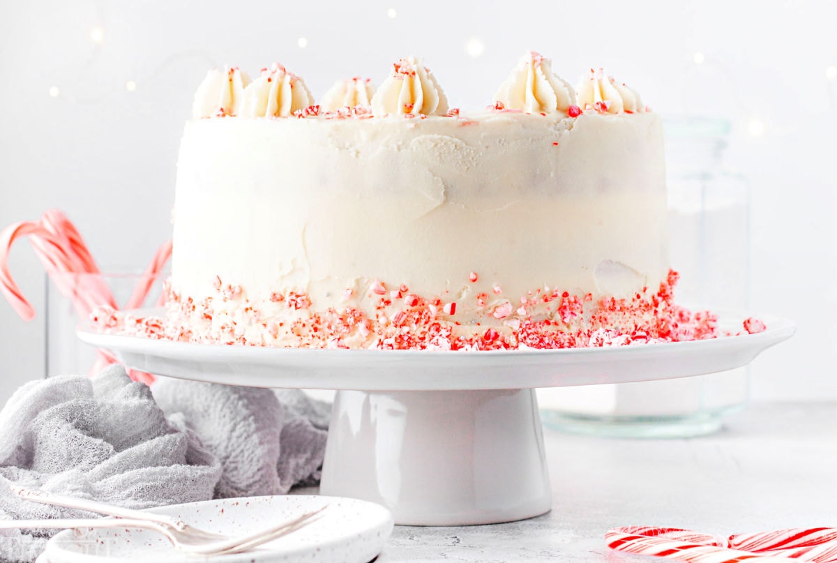 whole peppermint cake on a white cake stand with candy canes crumbles around the base.