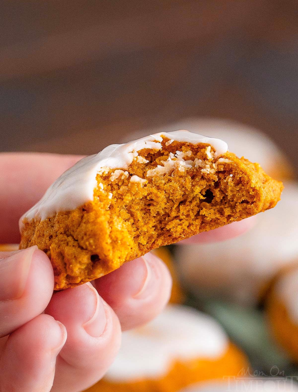 pumpkin oatmeal cookie with a bite taken out of it being held up over a plate of cookies.