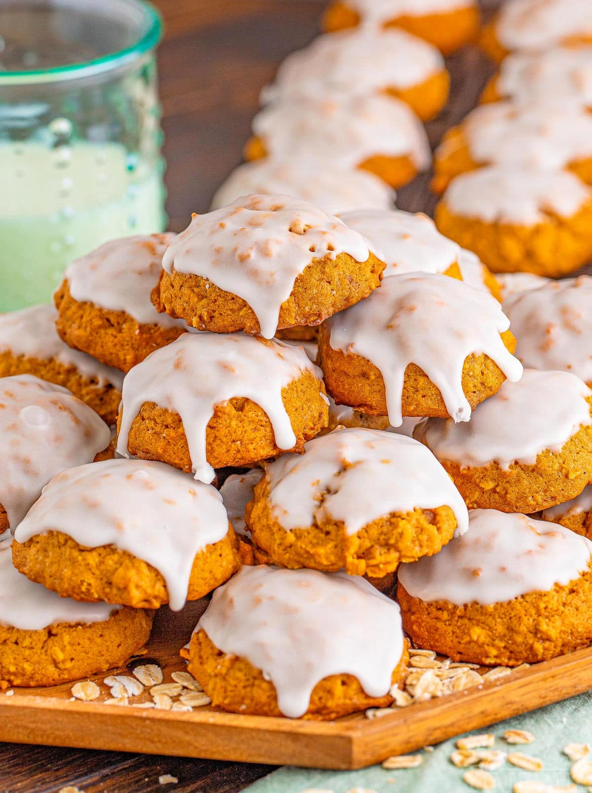 wood board with pumpkin oatmeal cookies stacked on top. cookies are iced.