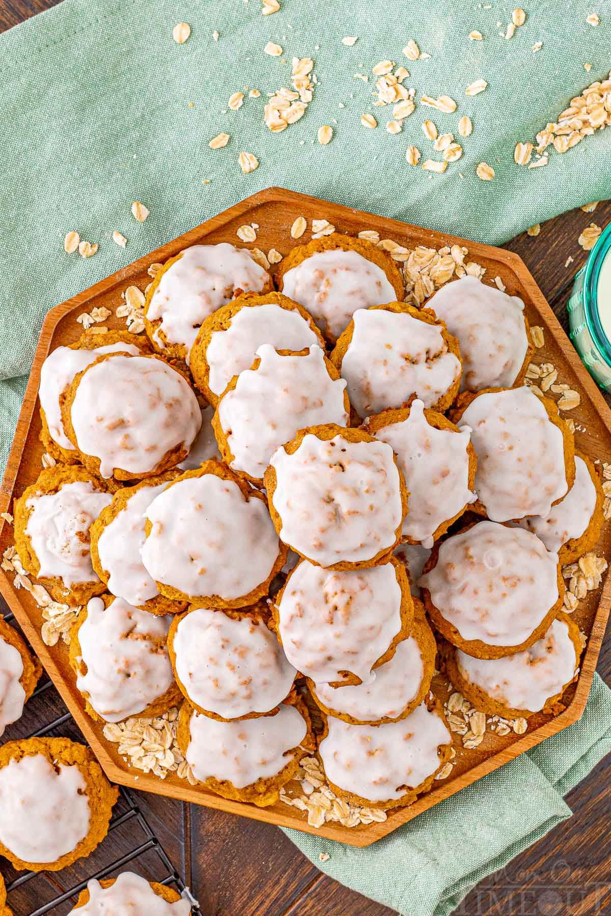 top down look at octagon shaped wood tray stacked high with pumpkin oatmeal cookies that have been iced. a green napkin is underneath the tray.