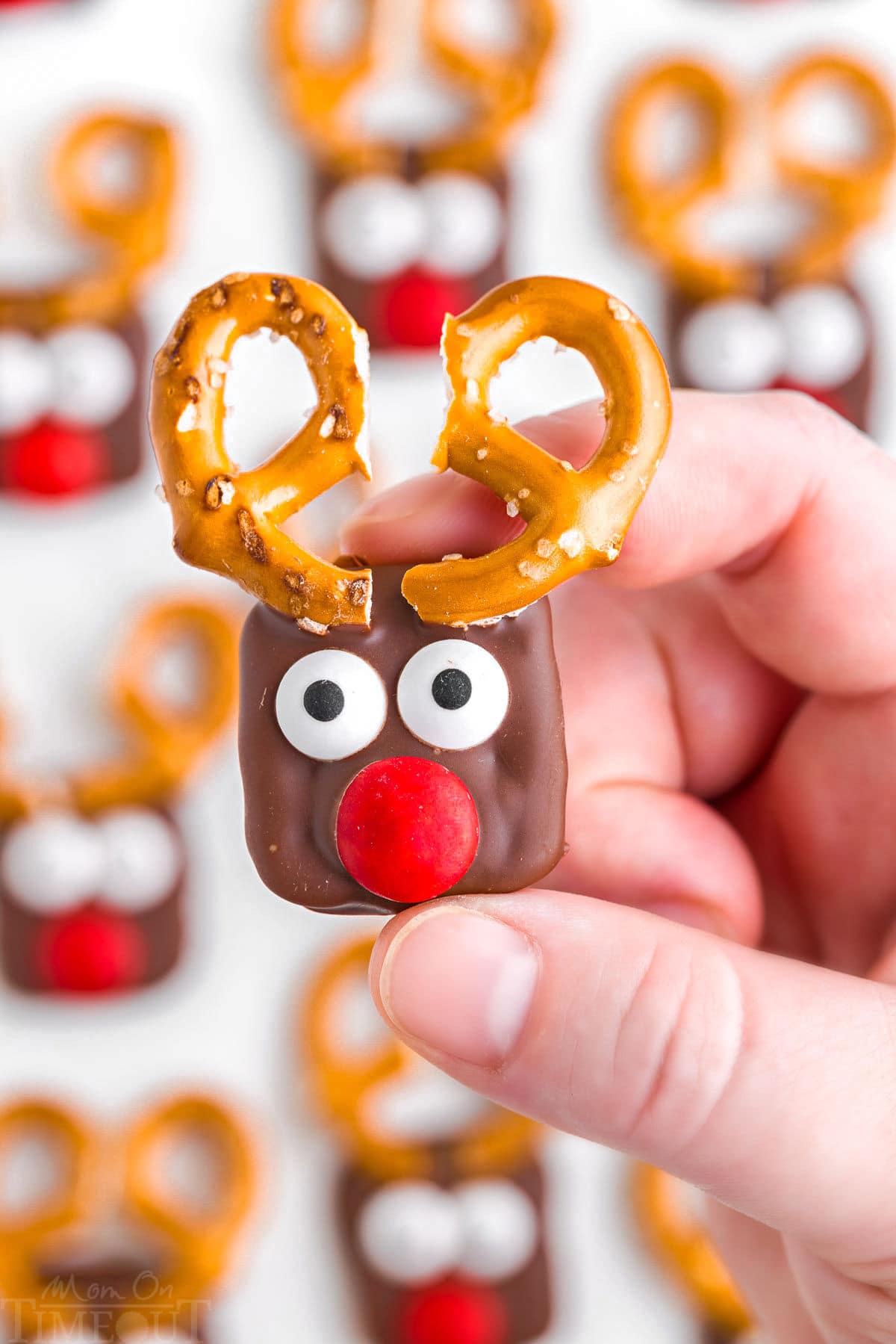 hand holding one of the reindeer pretzels over the rest of the treats setting up on parchment paper.