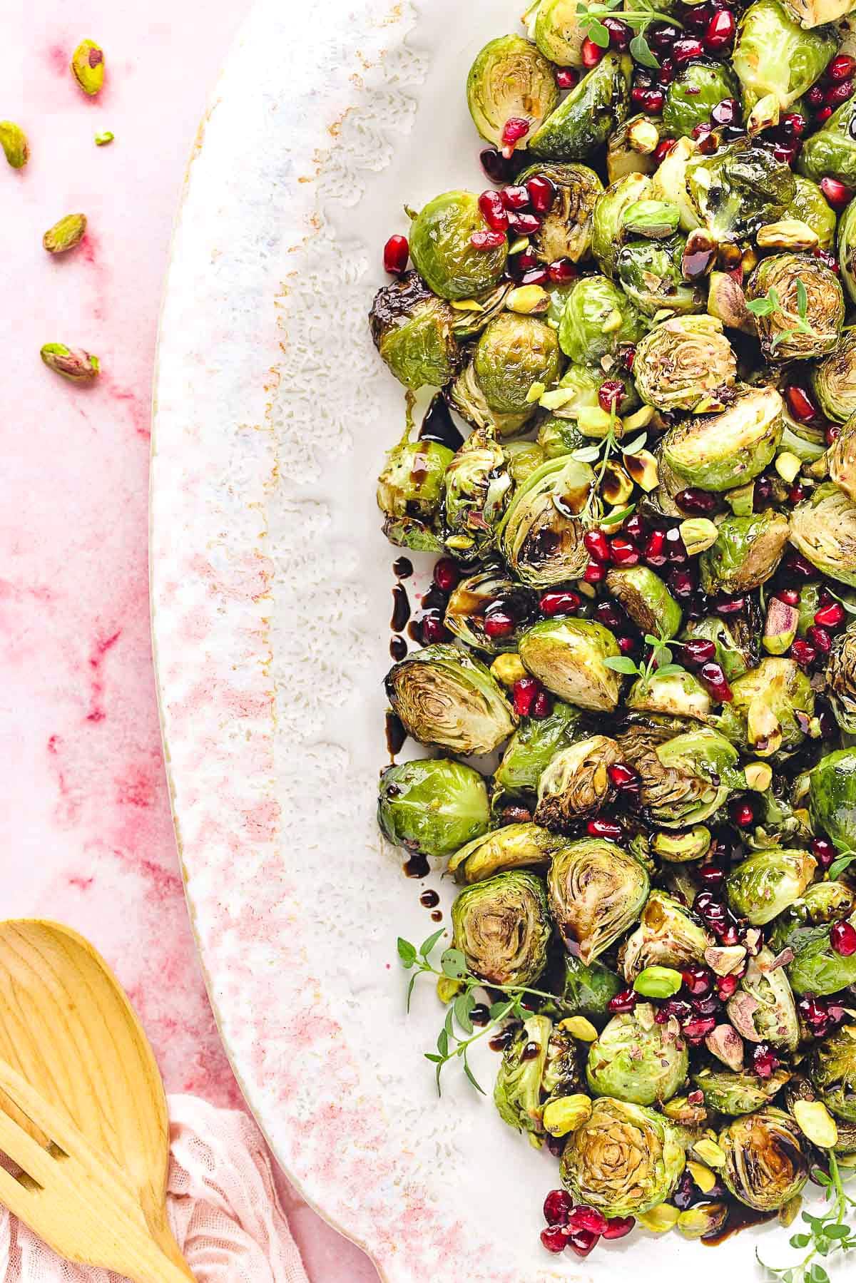 top down view of roasted brussels sprouts on a large white and pink platter. Pomegranate seeds and pistachios garnish the gorgeous dish.