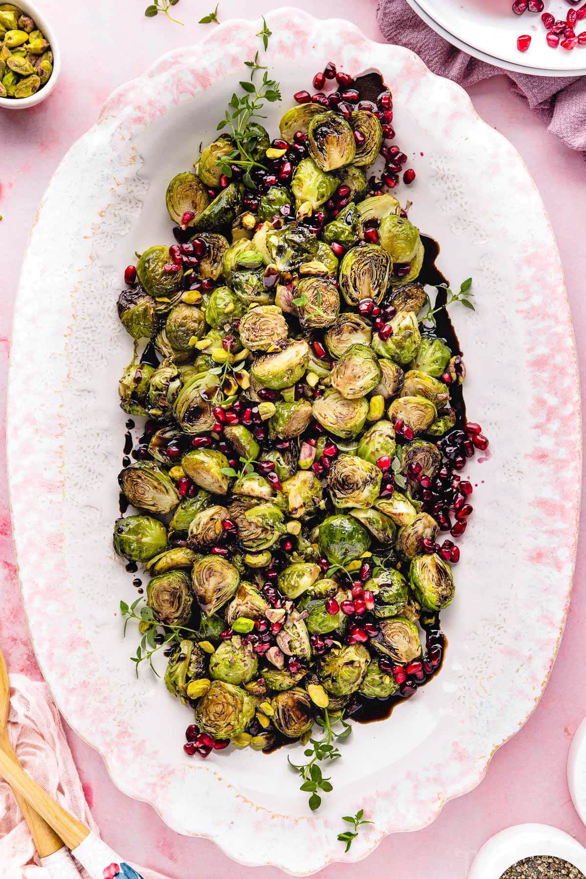 top down view of roasted brussels sprouts on a large white and pink platter. Pomegranate seeds and pistachios garnish the gorgeous dish.