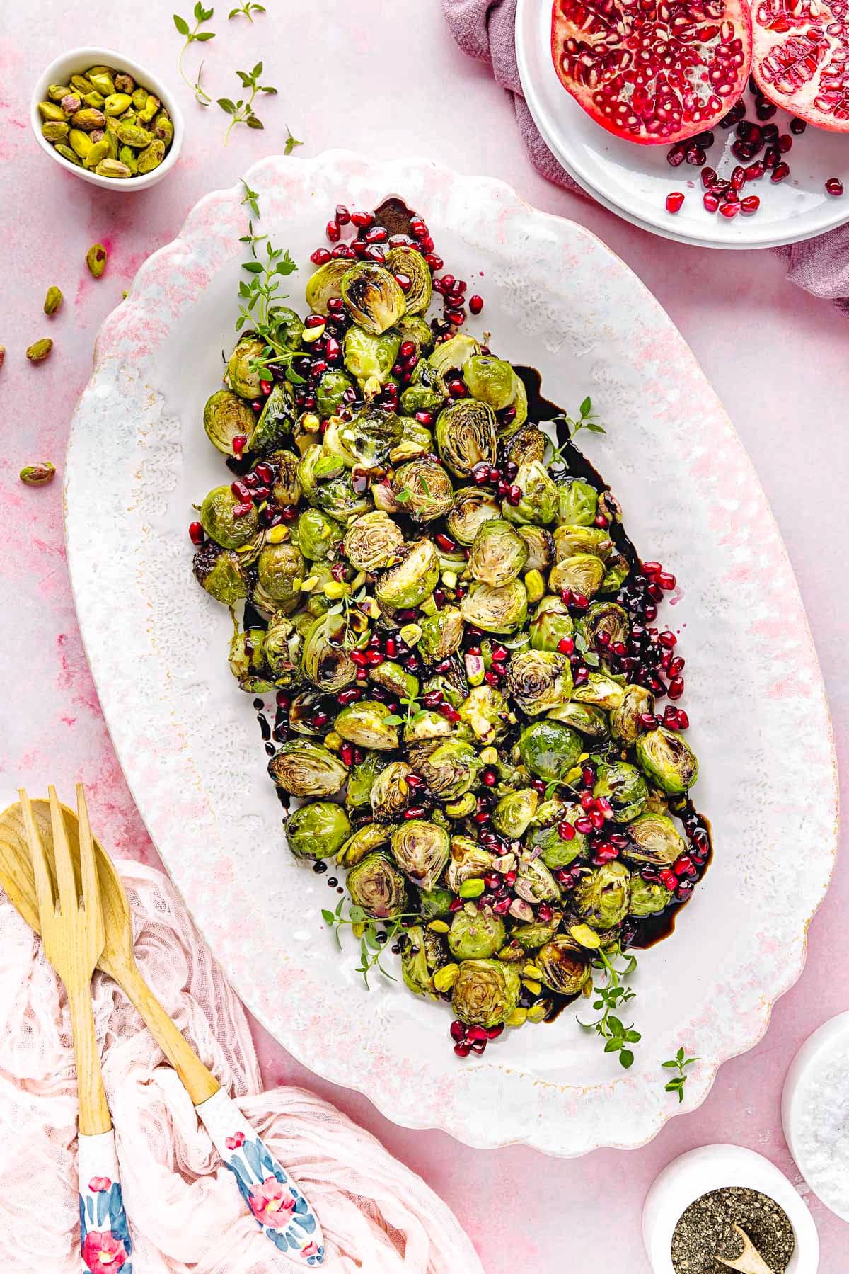top down view of roasted brussels sprouts on a large white and pink platter. Pomegranate seeds and pistachios garnish the gorgeous dish. 
