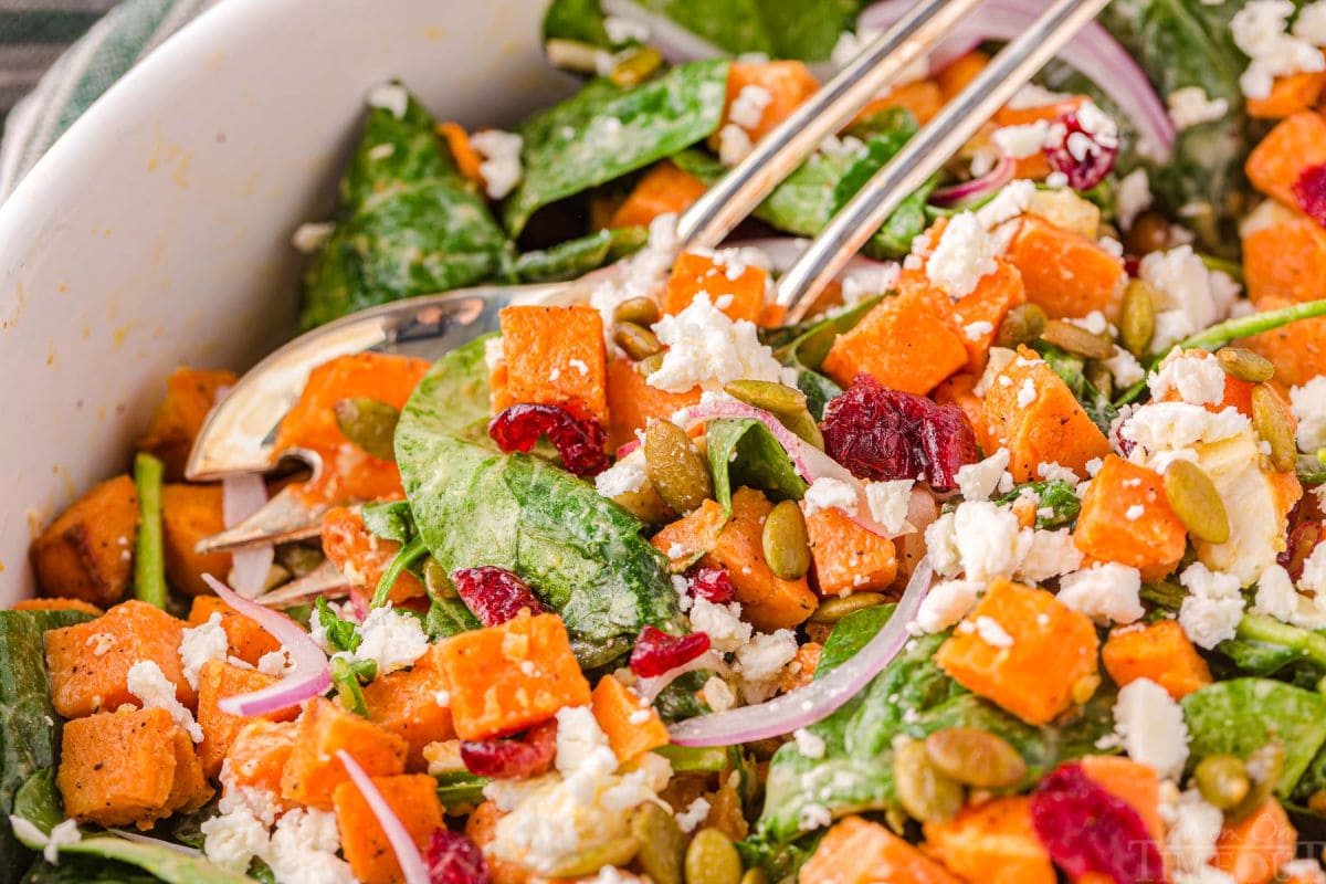 close up look at sweet potato salad in a large bowl with salad serving spoons.