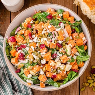 top down view of sweet potato salad in large serving bowl topped with dried cranberries and pepitas.