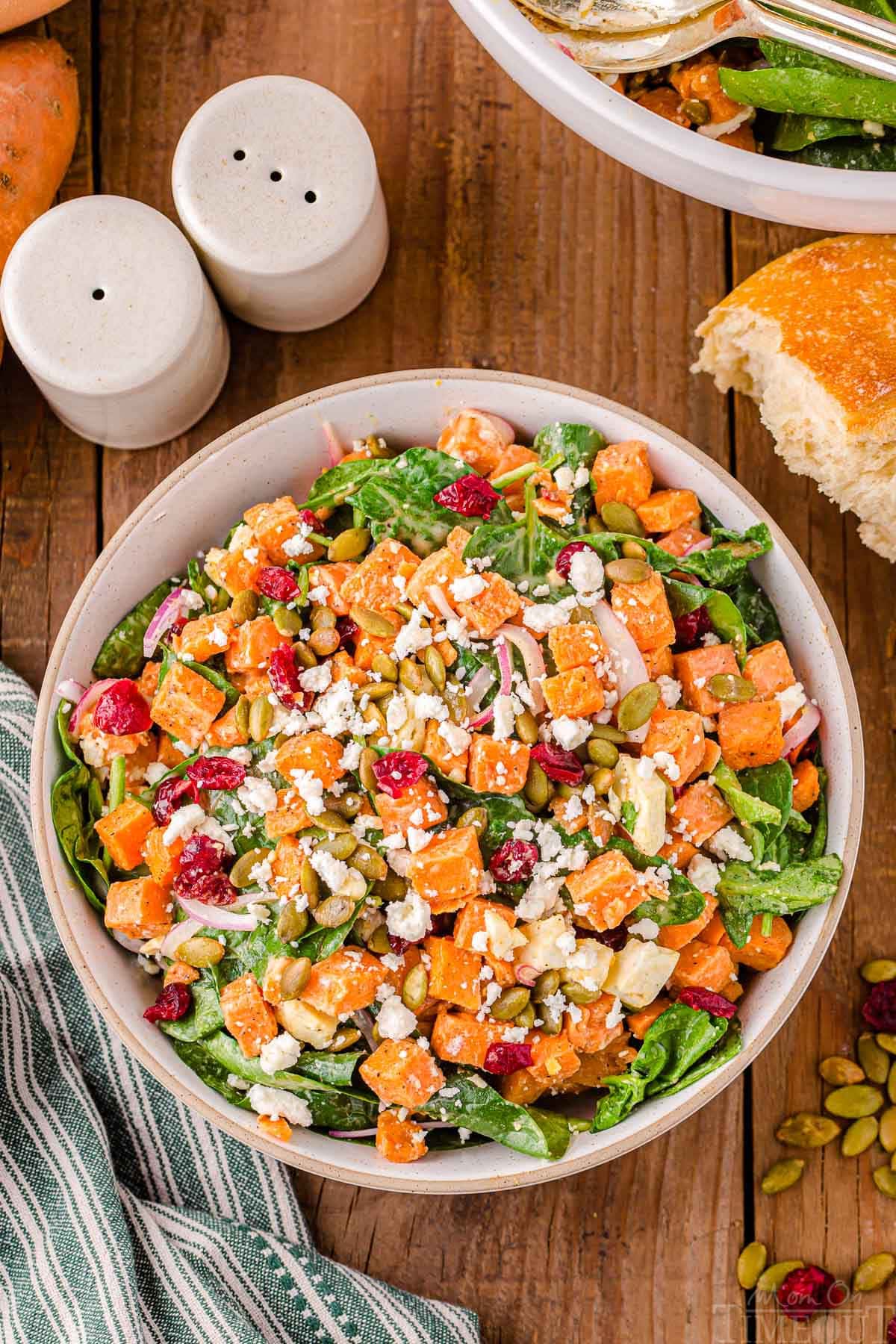 top down view of sweet potato salad in large serving bowl topped with dried cranberries and pepitas.