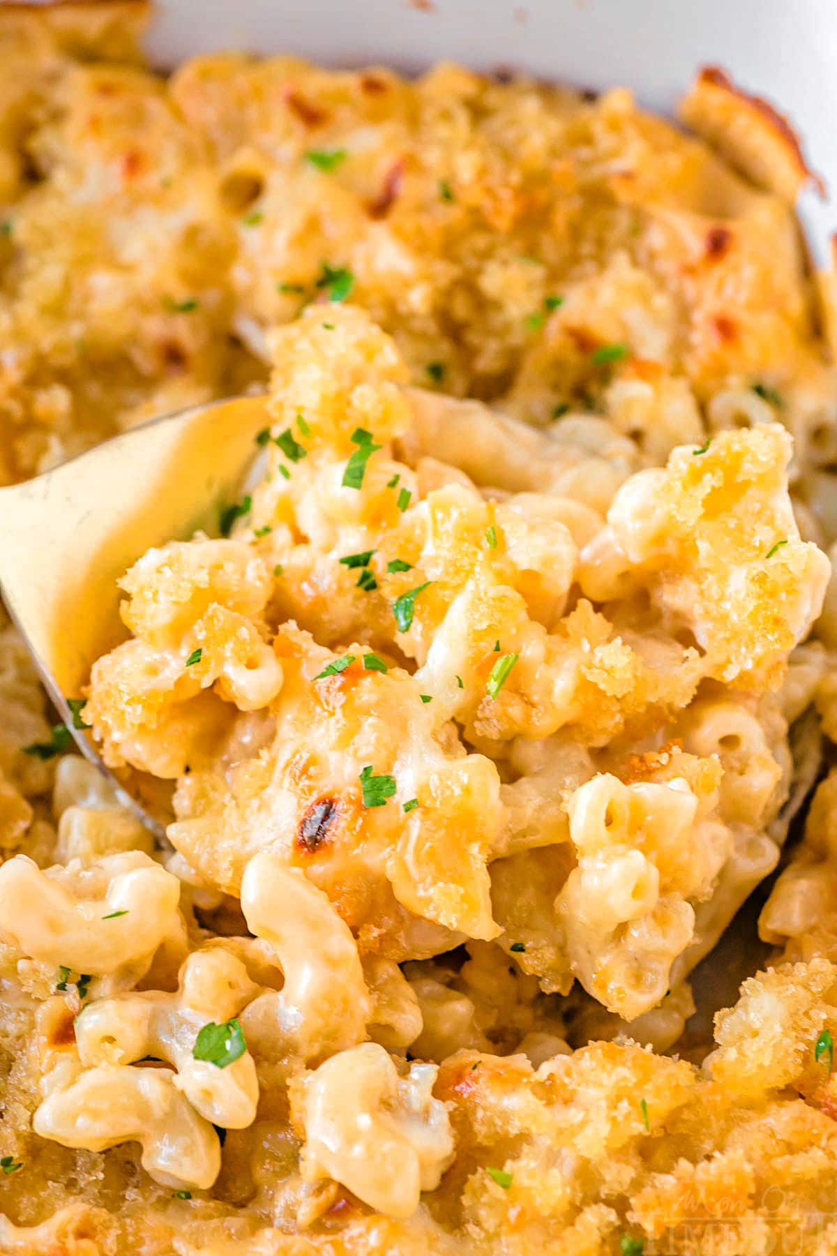 close up look at velveeta mac and cheese recipe in baking dish with gold spoon scooping it out of the dish.