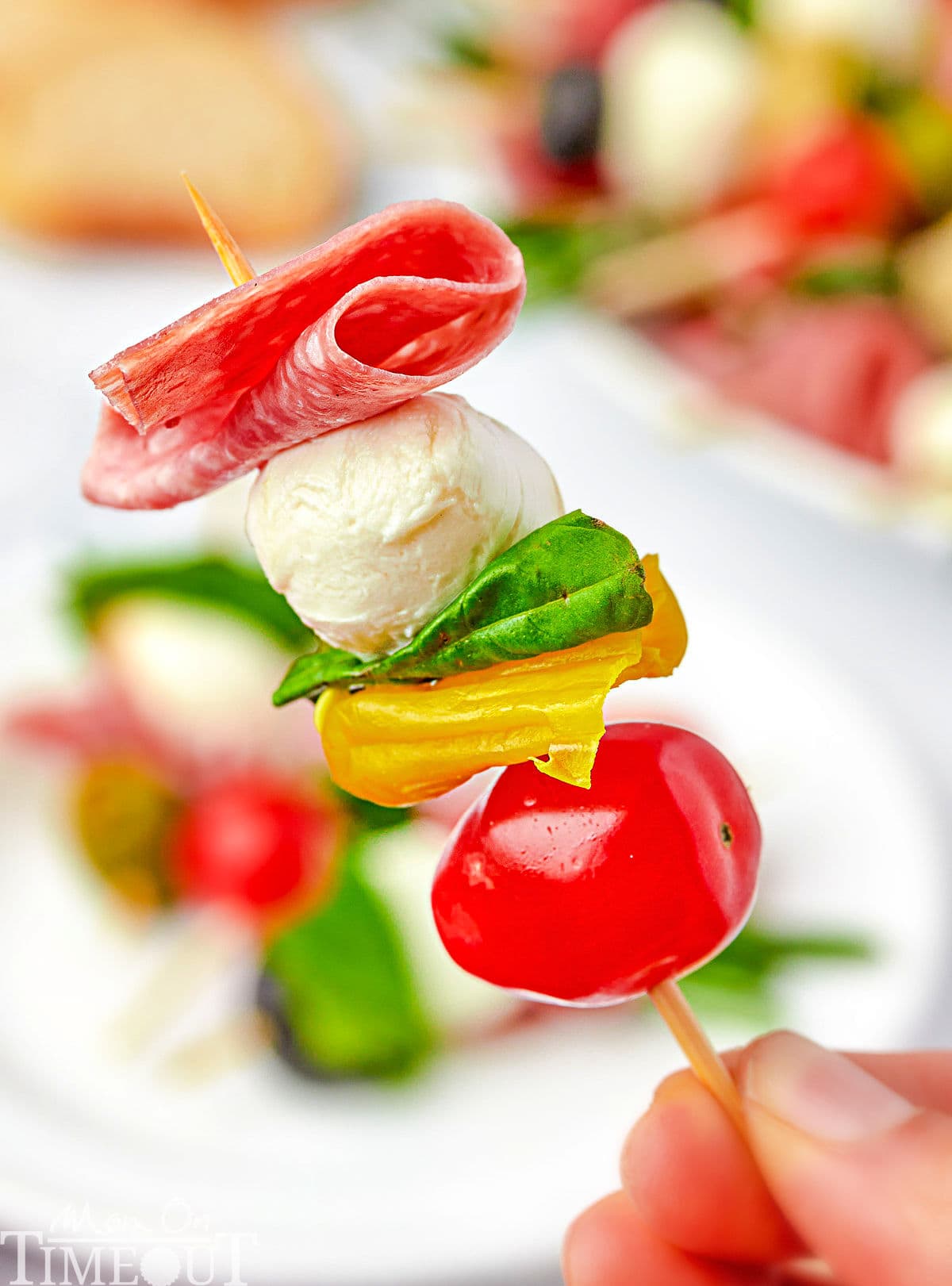 one antipasto skewer being held up over a plate.