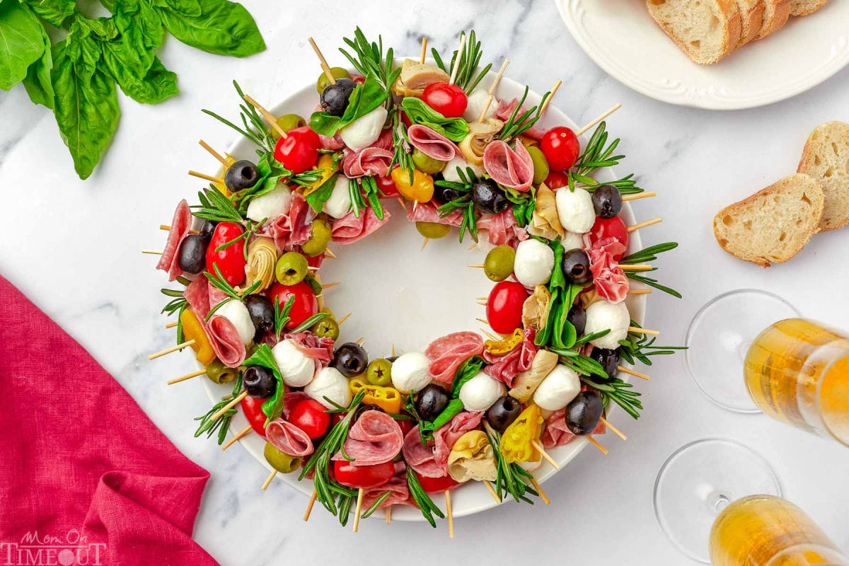 top down view of antipasto charcuterie wreath on a round white plate garnished with rosemary and basil.