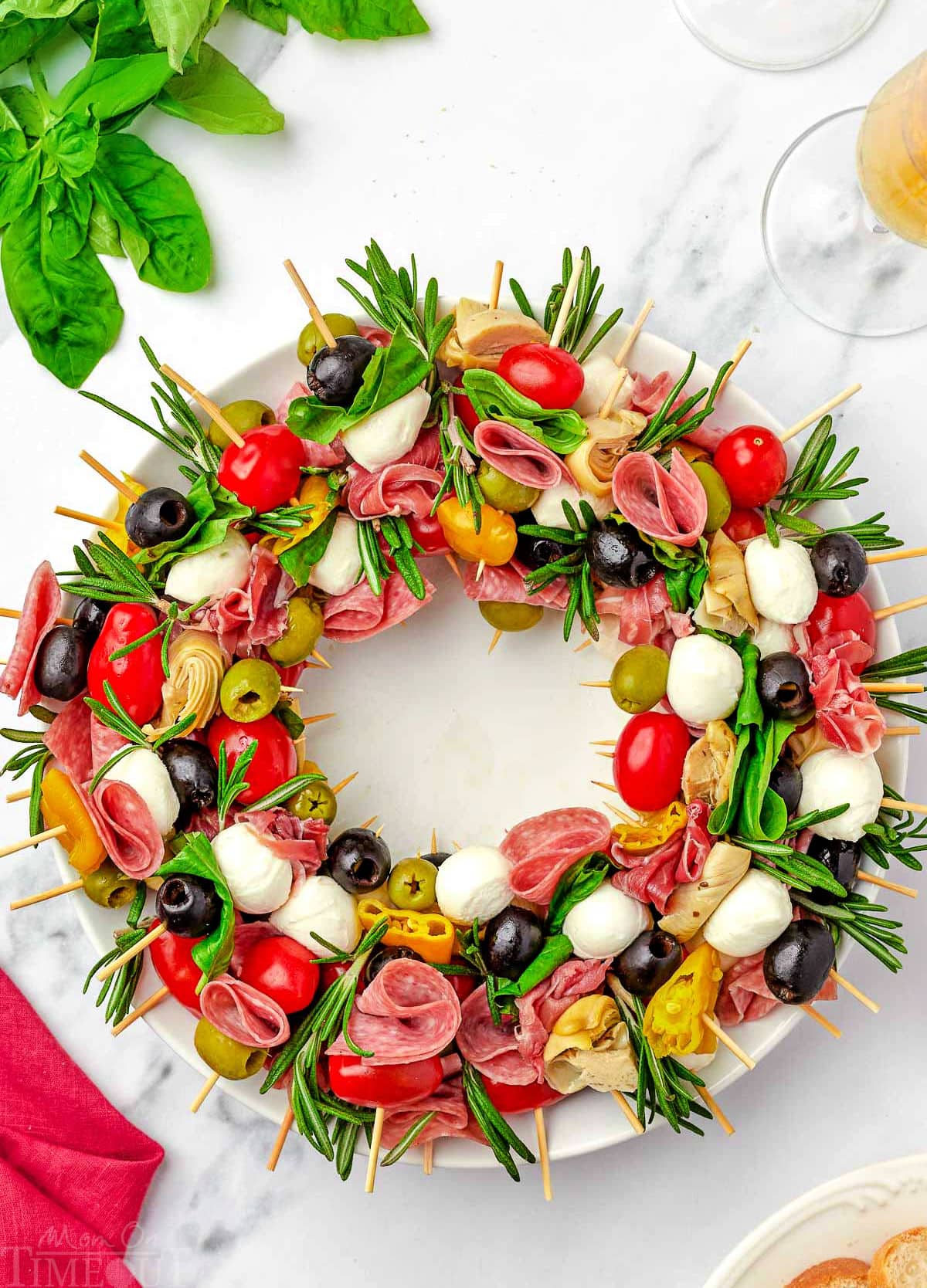 top down view of antipasto charcuterie wreath on a round white plate garnished with rosemary and basil.