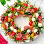 top down view of antipasto charcuterie wreath on a round white plate garnished with rosemary and basil.