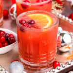 two christmas cocktails on a silver serving platter garnished with fresh cranberries and orange slices.