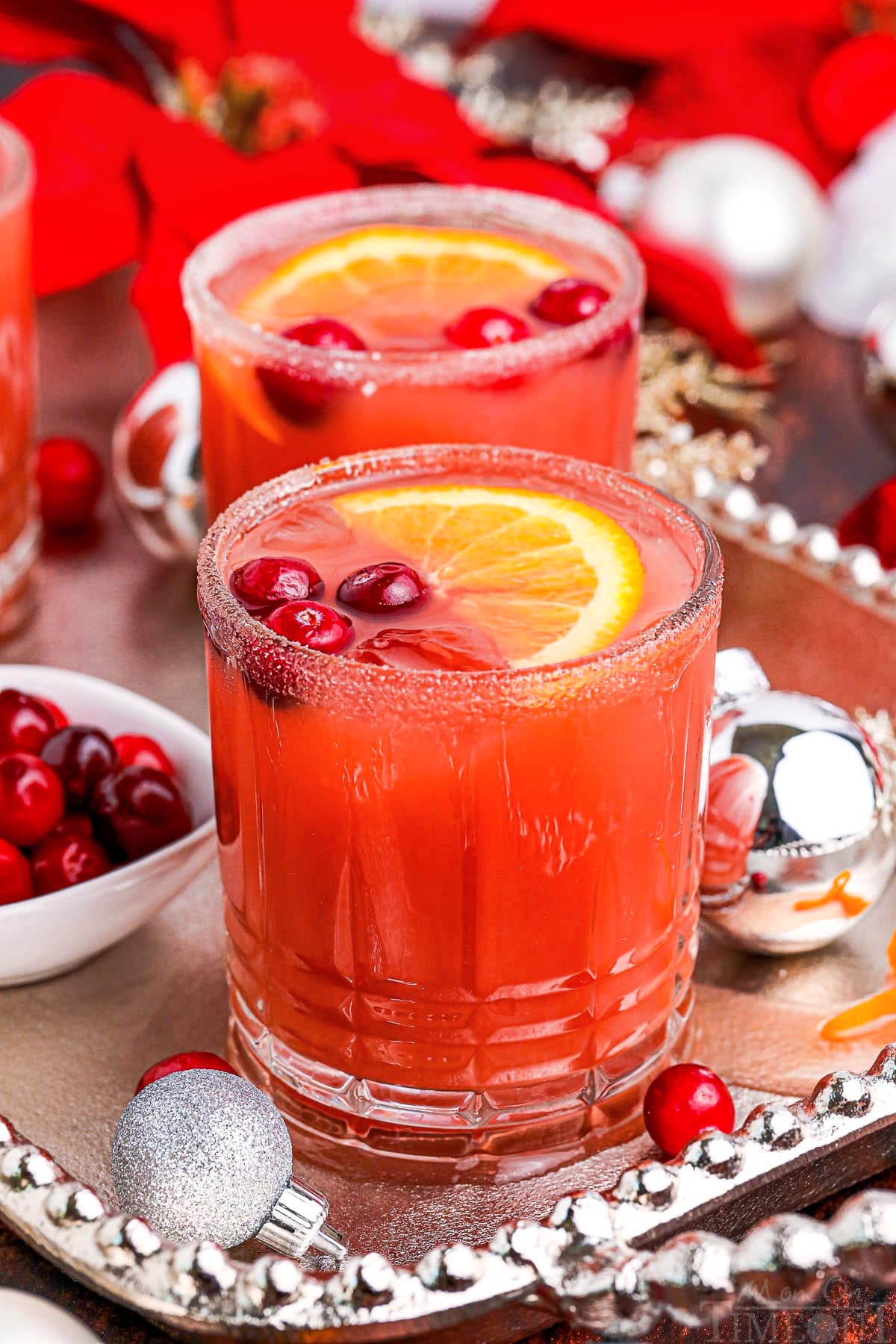 two christmas cocktails on a silver serving platter garnished with fresh cranberries and orange slices.