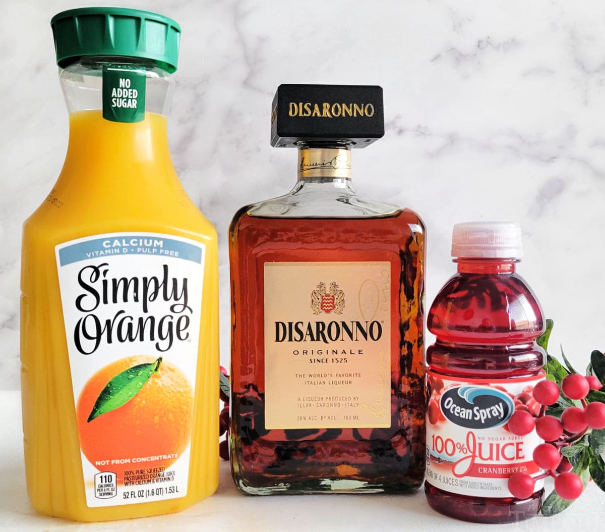 orange juice, amaretto and cranberry juice sitting on white surface ready to be used in christmas cocktail recipe.