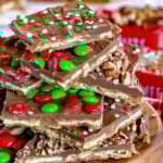 Square pieces of Christmas Crack cut and stacked on a round wood board. The toffee is topped with candy and sprinkles.