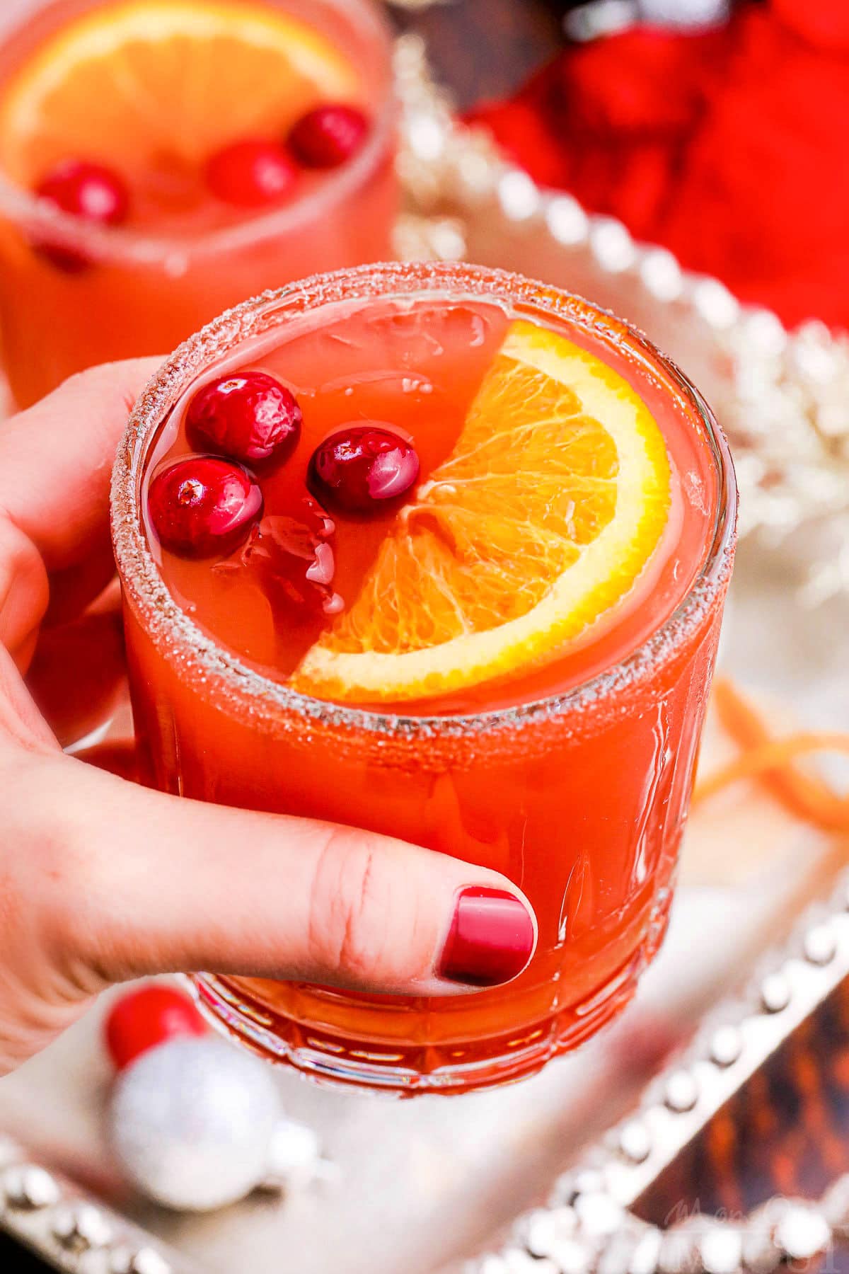 hand holding glass of christmas cocktail made with cranberry juice, orange juice and amaretto.