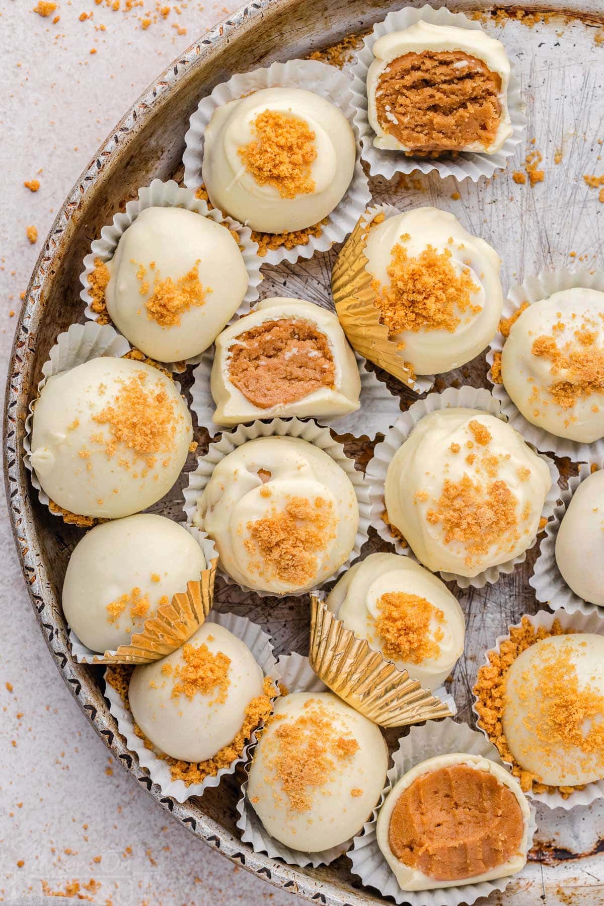 gingerbread truffles in white paper cups with gingersnap cookies crumbles sprinkles on top of the white chocolate coating. three of the truffles have a bite out of it.