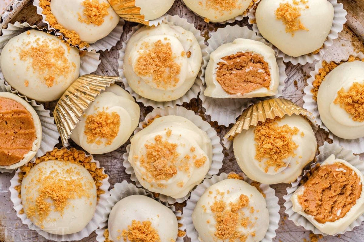 top down view of easy gingerbread truffles in white paper cups sitting on a silver parchment tray. three of the truffles have been bitten in half.