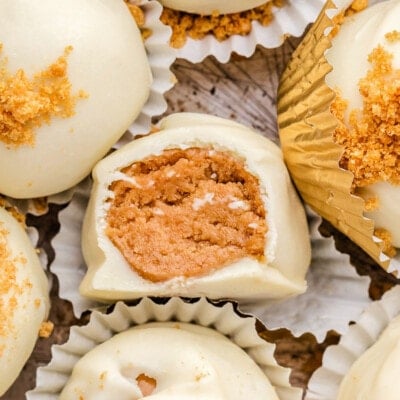 gingerbread truffles in white paper cups with gingersnap cookies crumbles sprinkles on top of the white chocolate coating. one truffle has a bite out of it.